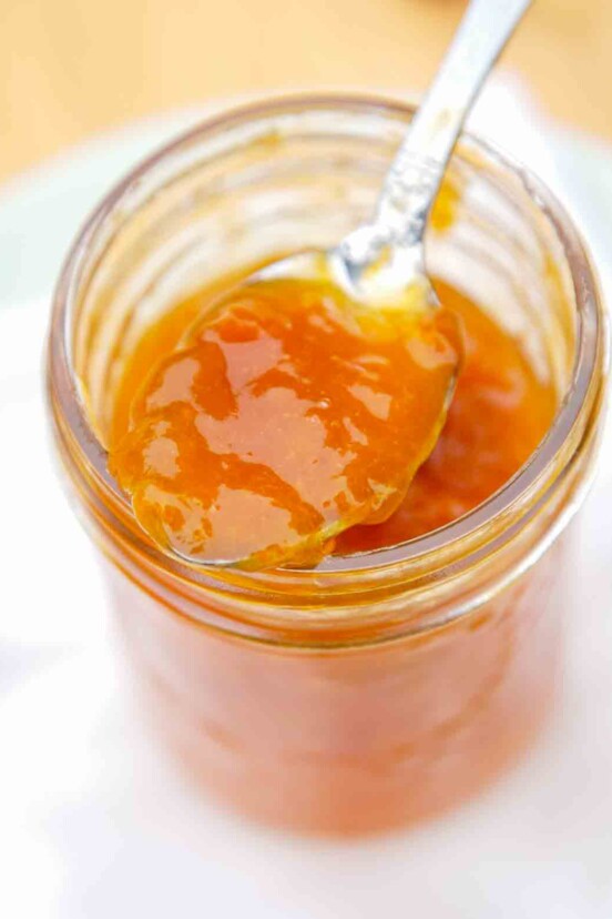 A jelly jar filled with apricot jam and a spoon resting on top.
