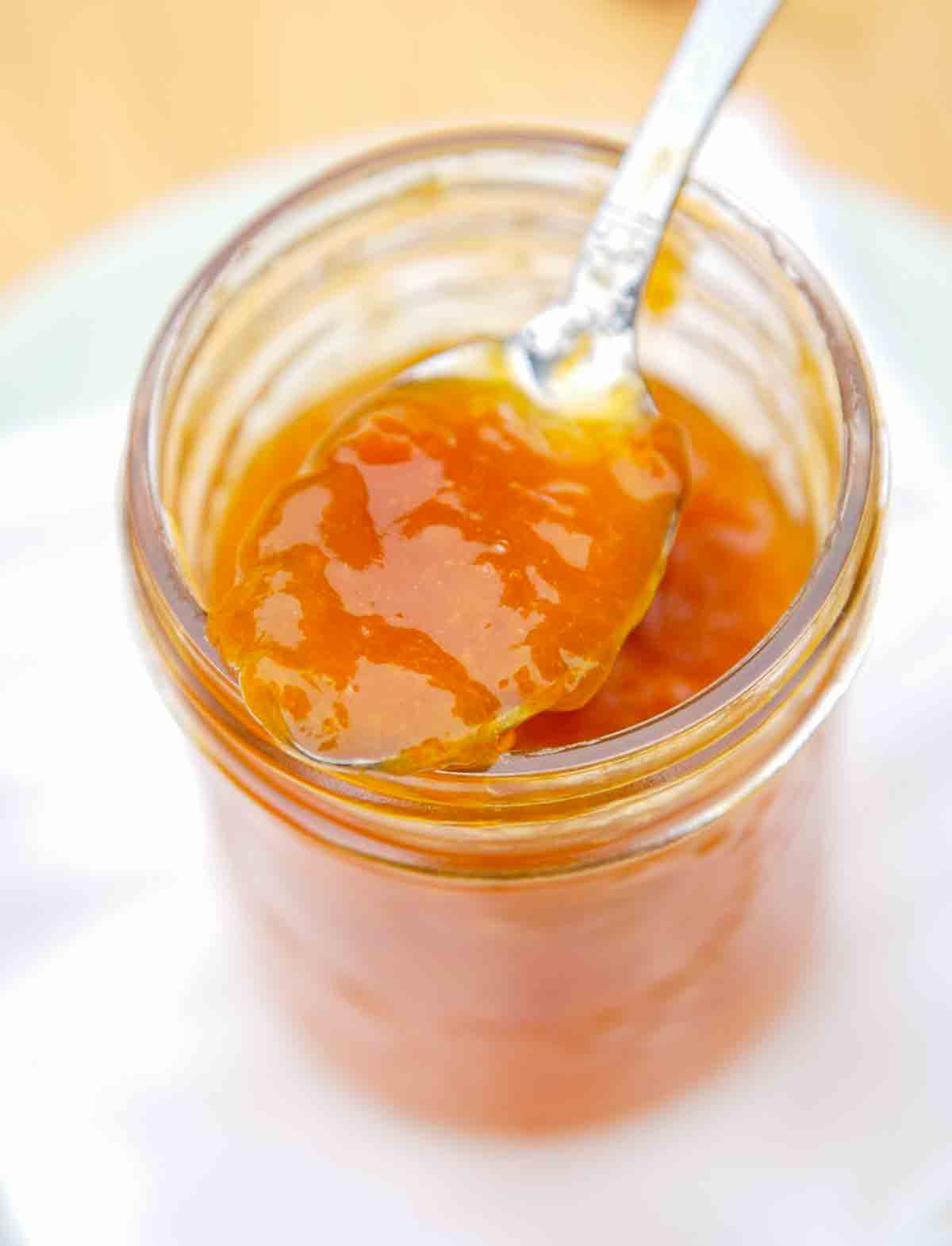 A jelly jar filled with apricot jam and a spoon resting on top.