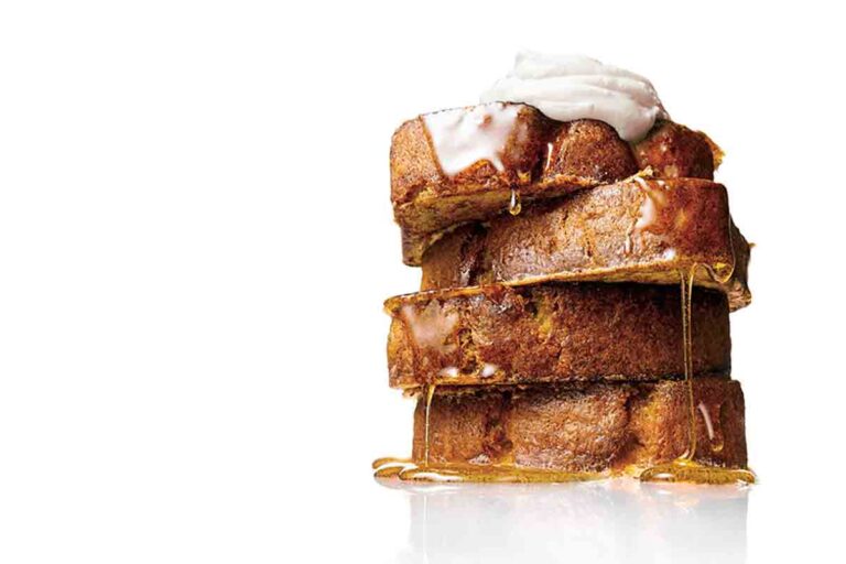 A stack of four slices of banana bread French toast dripping with maple syrup and topped with sour cream.