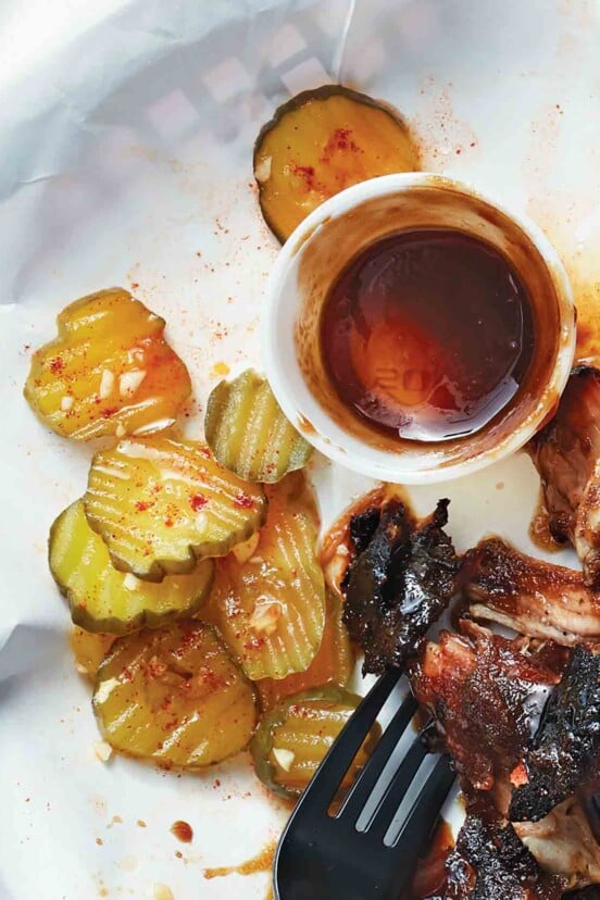 A pile of barbecue pickles next to some barbecued meat and a fork.