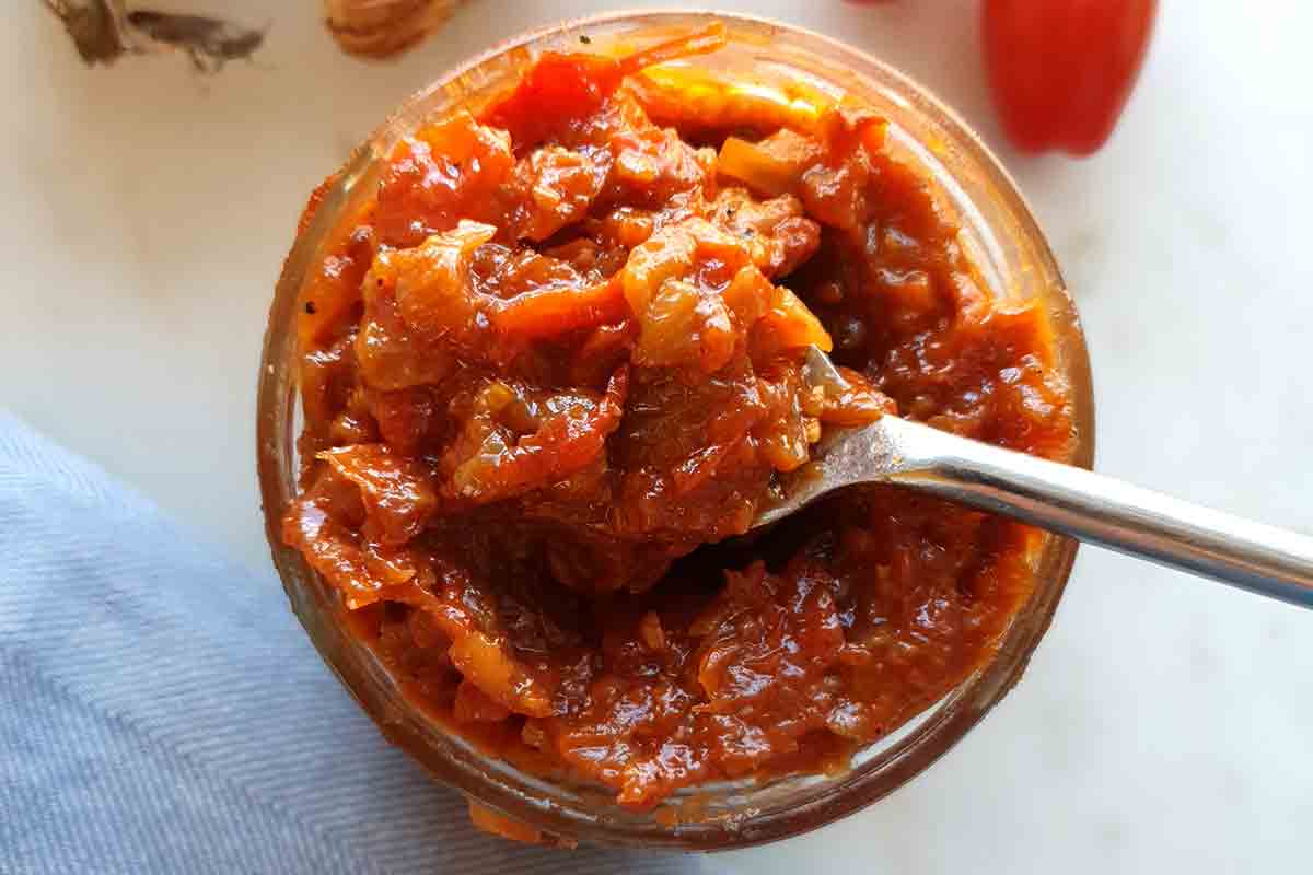 A jar of caramelized onion and tomato jam with a spoon resting inside it.
