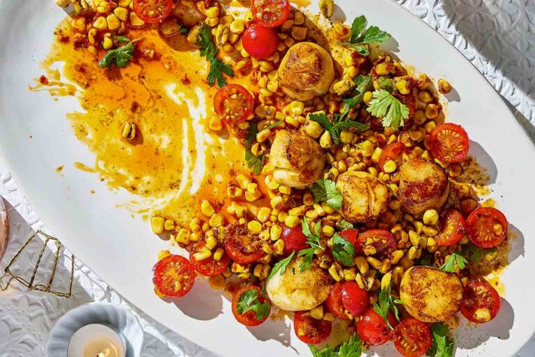 A white oval platter half-filled with charred corn and scallop salad.
