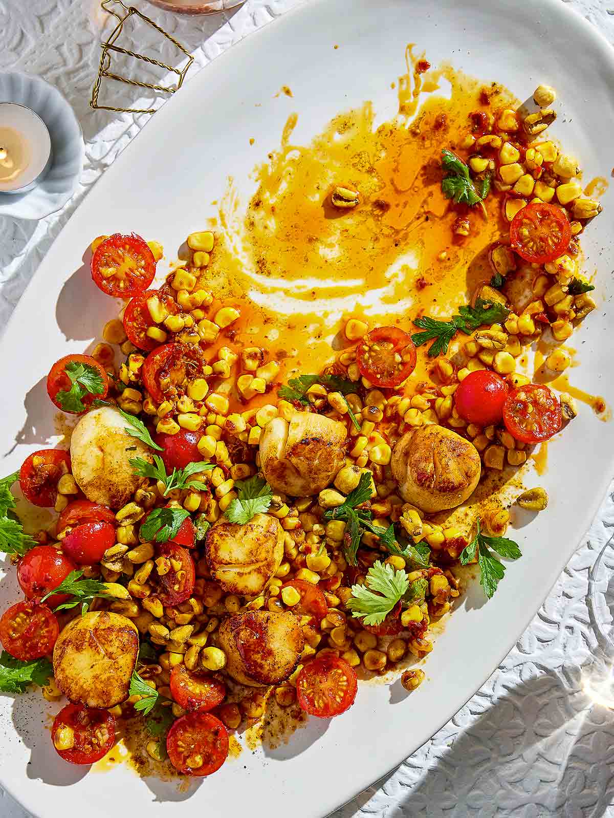 A white oval platter half-filled with charred corn and scallop salad.