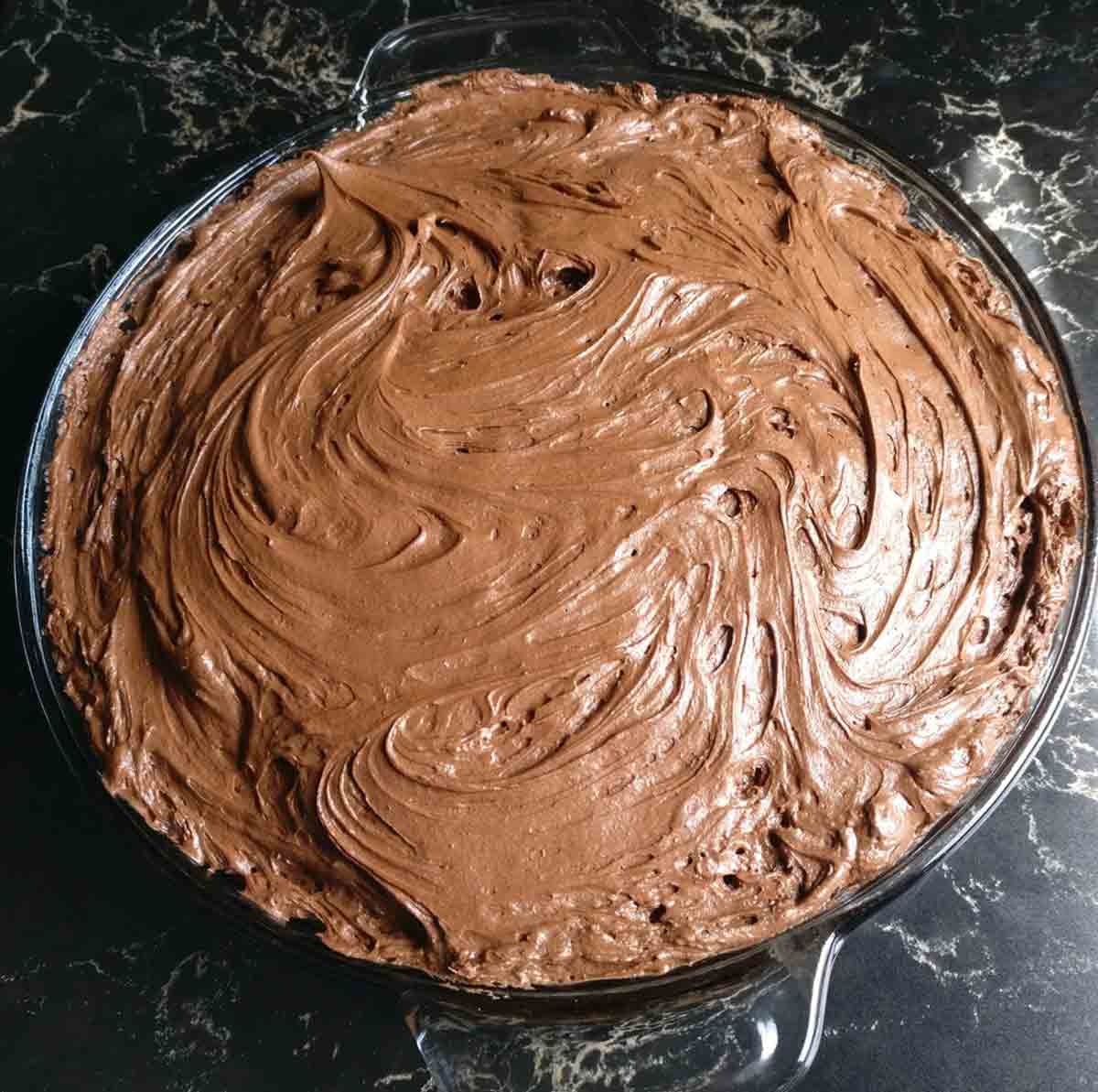 A chocolate wacky cake with chocolate frosting in a glass pie plate.