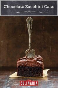 En fyrkant av chokladzucchini-kaka med smörkrämglasyr på en fyrkant av pergament med en gaffel som står upp i mitten av kakan.