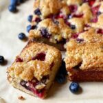 A rectangular easy mixed berry snacking cake with one piece cut from it and blueberries on the side.