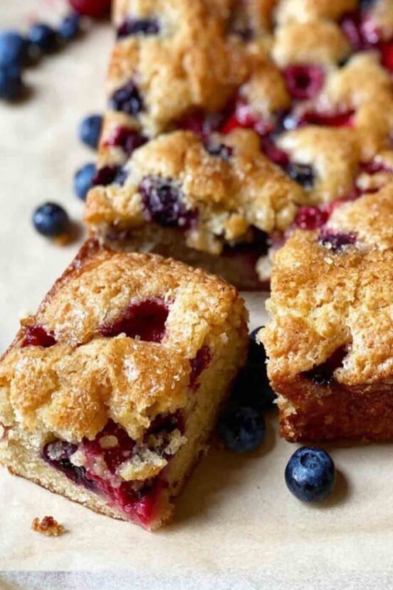 A rectangular easy mixed berry snacking cake with one piece cut from it and blueberries on the side.
