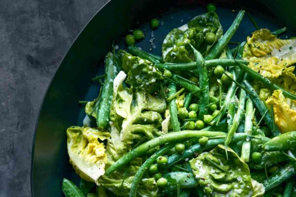 A black bowl filled with green beans, peas, and butter lettuce.