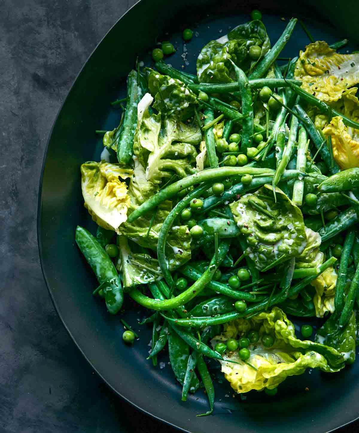 A black bowl filled with green beans, peas, and butter lettuce.