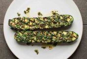 Two grilled zucchini halves on a white plate, topped with mint salsa.