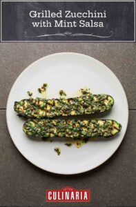 Two grilled zucchini halves on a white plate, topped with mint salsa.