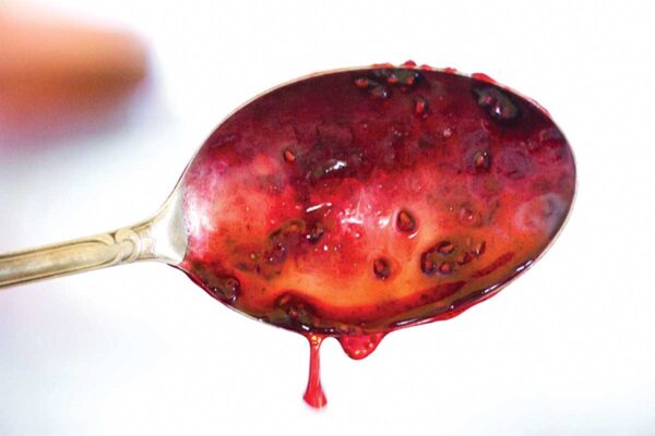 A spoon with raspberry jam dripping off of it.