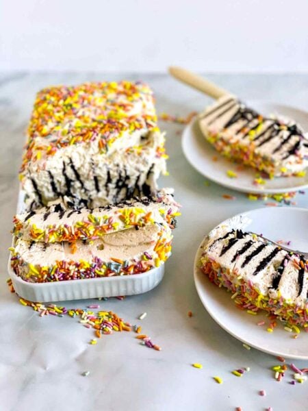 A partially sliced icebox cake with condensed milk whipped cream and slices on two plates.