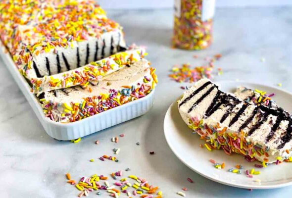 A slice of icebox cake with condensed milk whipped cream on a plate with the rest of the cake nearby and a container of sprinkles in the background.