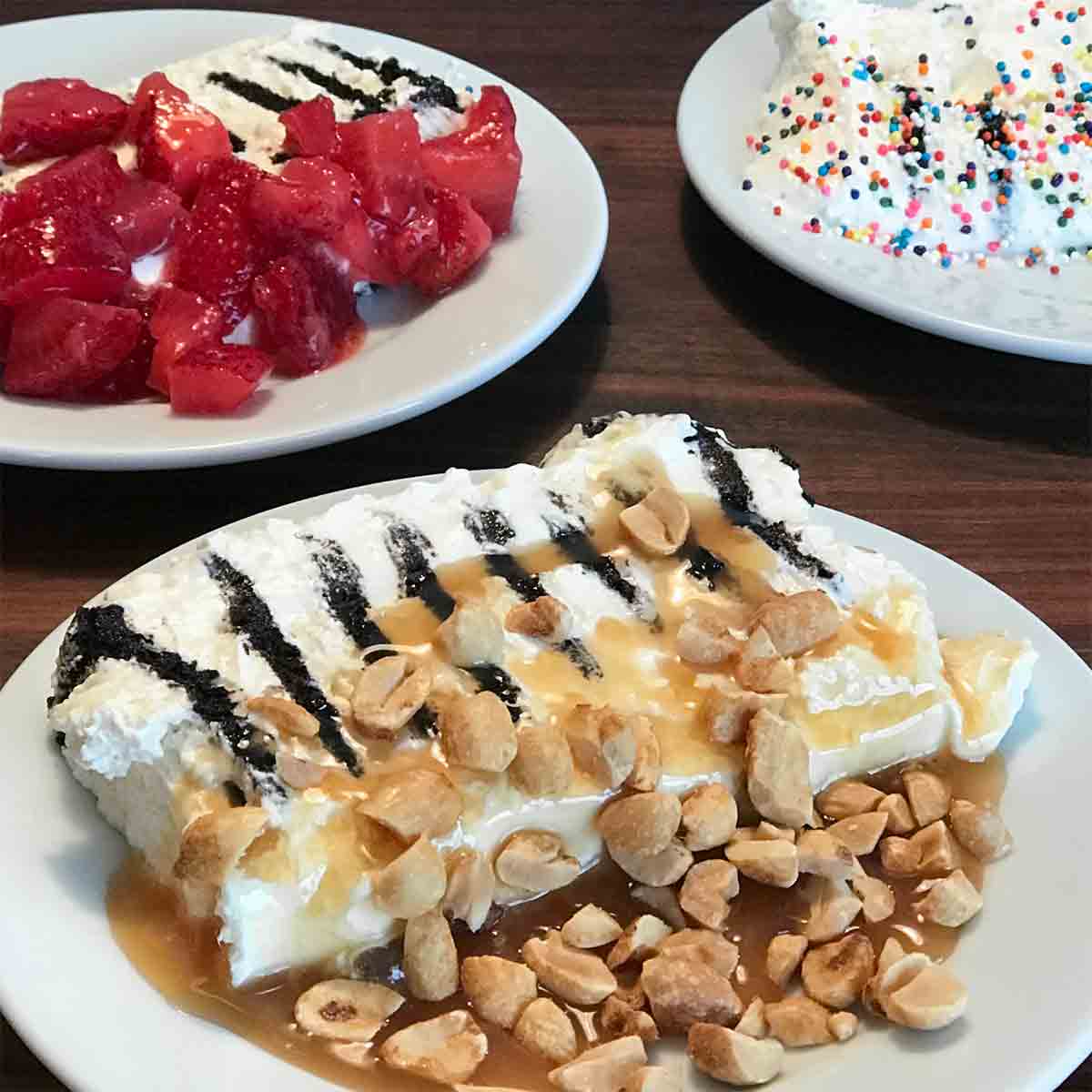 A slice of icebox cake on white plate, topped with peanuts and caramels sauce and another slice topped with strawberries.