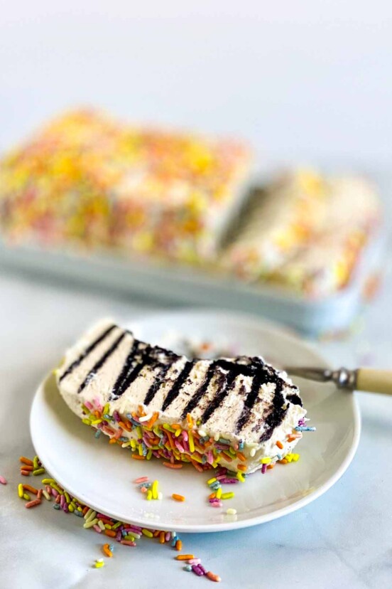 A slice of icebox cake with condensed milk whipped cream and sprinkles with the rest of the cake in the background.