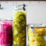 Three jars of Israeli pickles, one with cauliflower, one with cucumbers, and one with red onion.