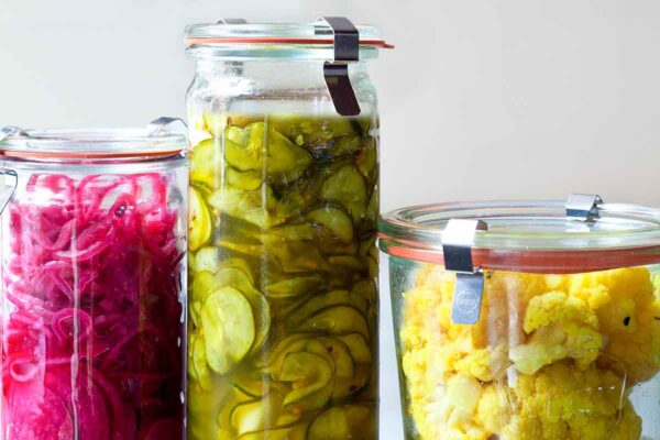 Three jars of Israeli pickles, one with cauliflower, one with cucumbers, and one with red onion.
