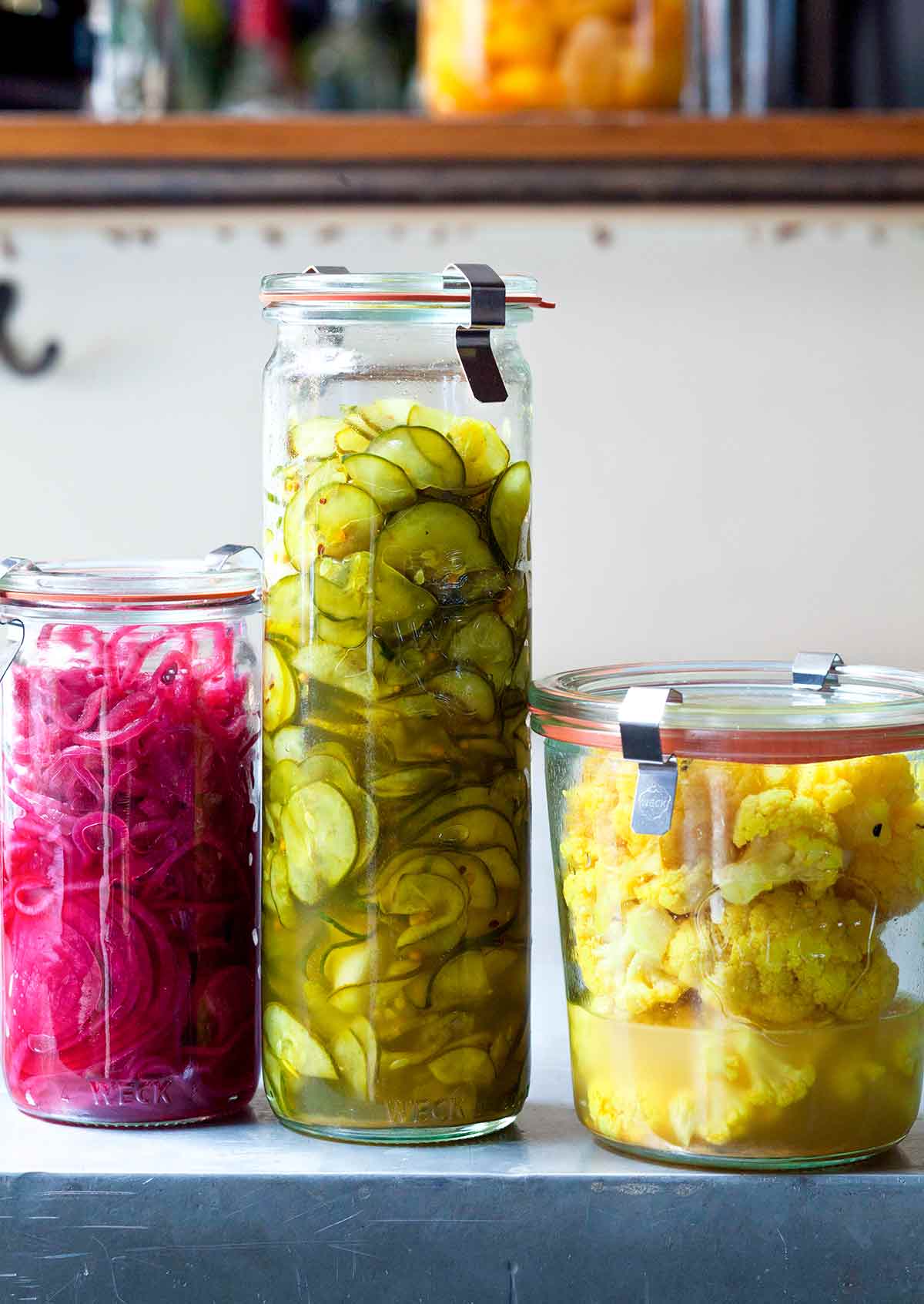 Tre burkar israelisk pickles, en med blomkål, en med gurka och en med rödlök.