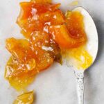 A spoonful of mixed citrus marmalade spilling over onto a grey marble surface.