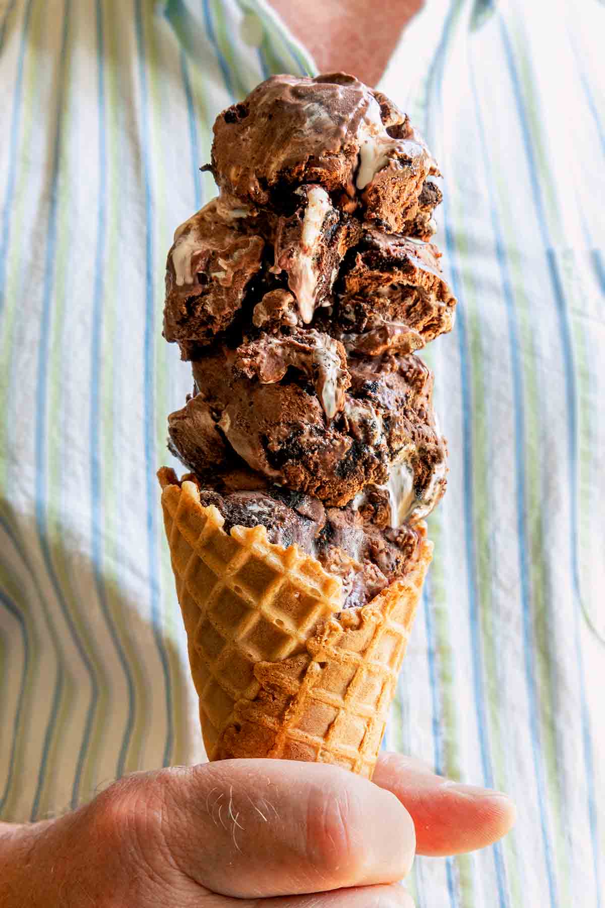 A man holding a waffle cone filled with four scoops of chocolate Oreo ice cream.