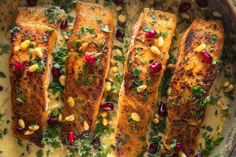 Four pieces of pan seared salmon in a sweet tahini sauce, topped with pomegranate and pine nuts.