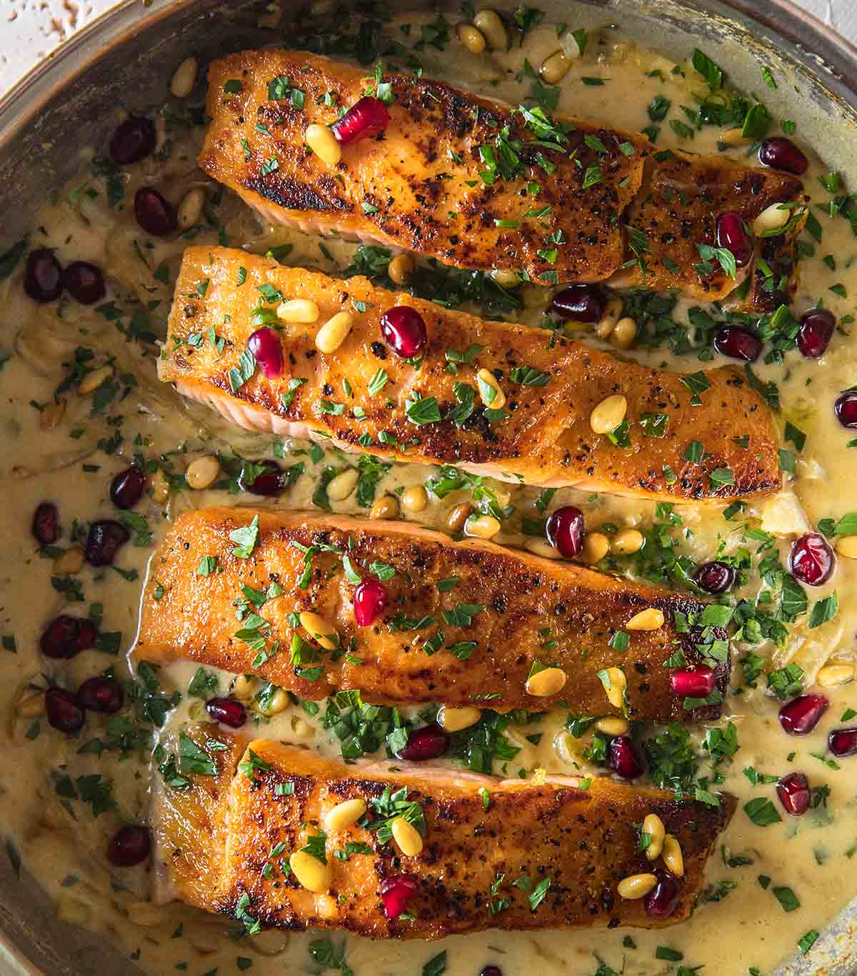 Four pieces of pan seared salmon in a sweet tahini sauce, topped with pomegranate and pine nuts.