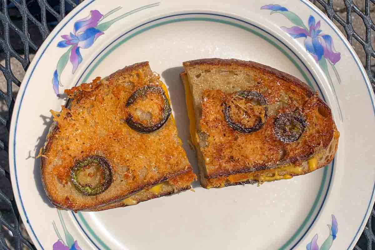 A halved Parmesan-crusted grilled cheese with jalapeños on a white decorative plate.