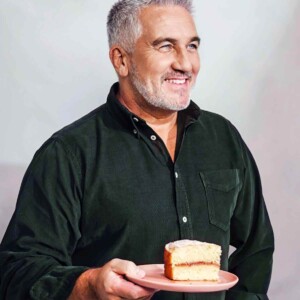 Paul Hollywood standing holding a piece of cake