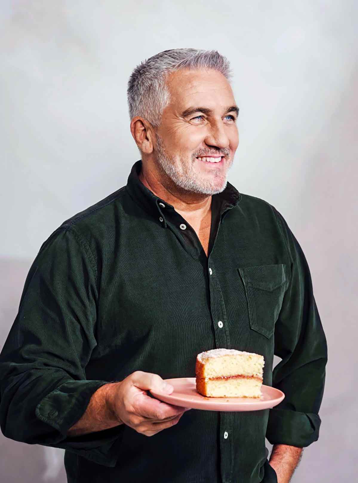 Paul Hollywood standing holding a piece of cake