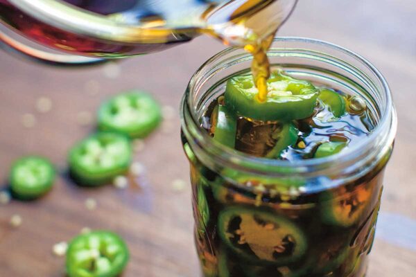 Pickling liquid being poured into a full jar of pickled jalapeno peppers.