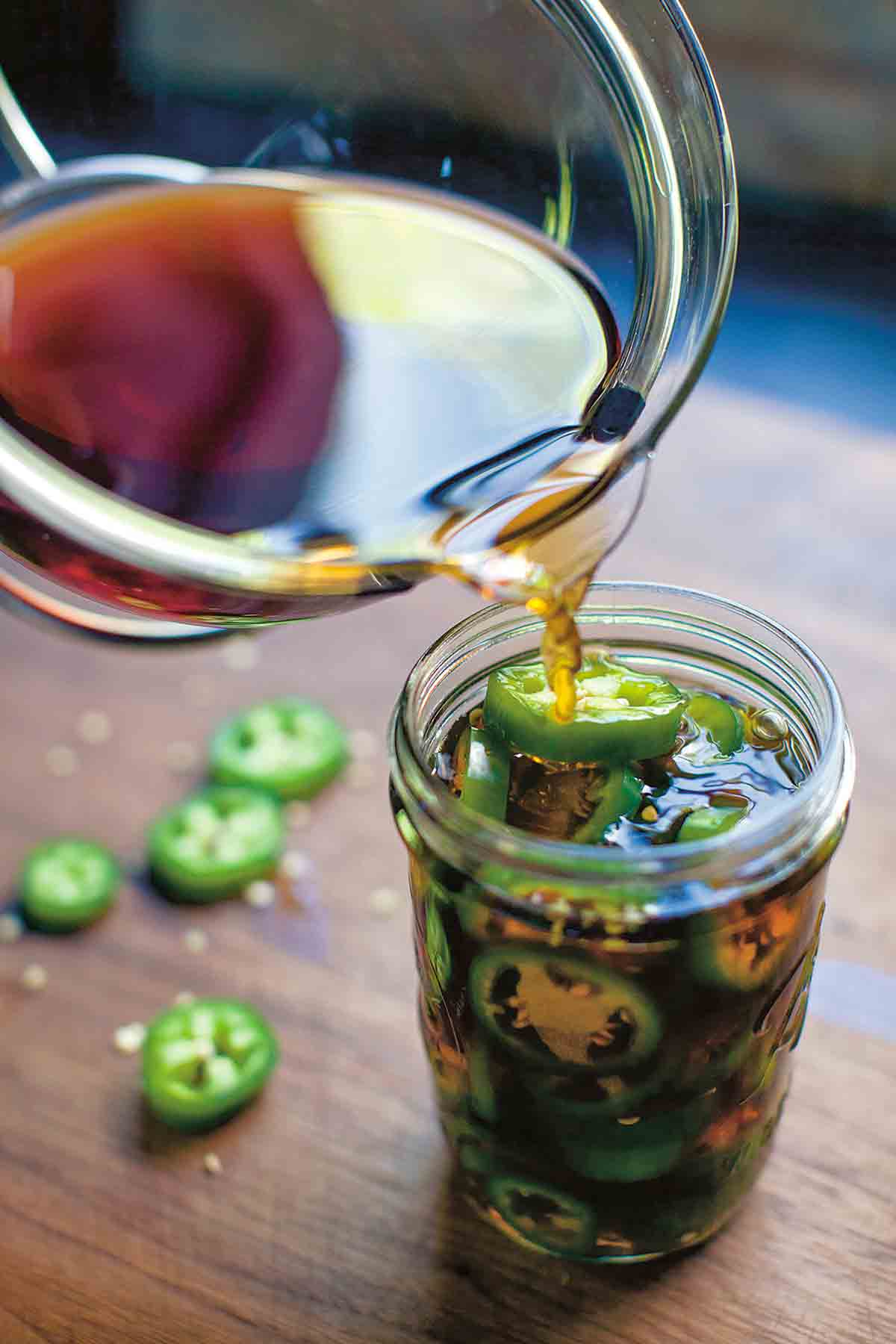 Pickling liquid being poured into a full jar of pickled jalapeno peppers.