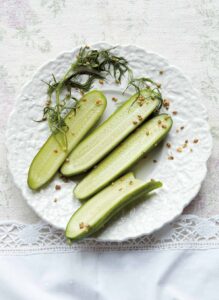 Three and a half quick dill pickles, dill seed, and a sprig of dill on a decorative white plate.