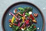 A round blue plate topped with rainbow chard salad, candied nuts, and creamy dressing.
