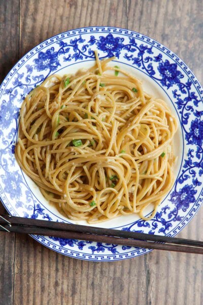 A blue and white bowl filled with San Francisco-style Vietnamese garlic noodles with a pair of chopsticks resting on the side of the bowl.