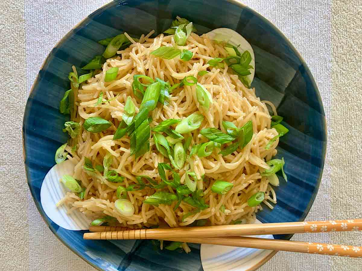 A blue bowl filled with San Francisco-style Vietnamese garlic noodles, topped with sliced scallions, and a pair of chopsticks on the side.