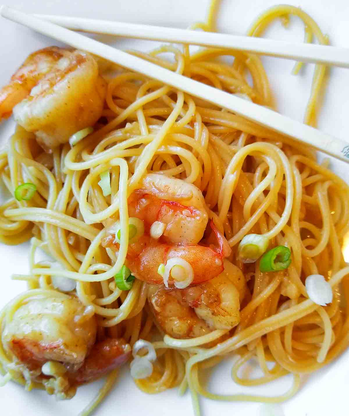 San Francisco-style Vietnamese garlic noodles with shrimp and scallions in a white bowl with chopsticks on the side.