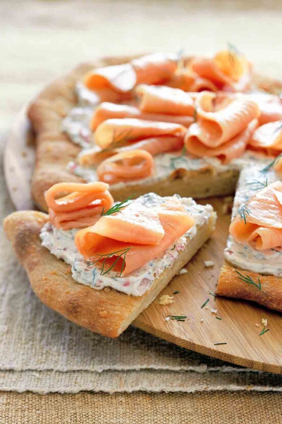 A smoked salmon pizza with cream cheese, red onion, and dill with one wedge cut out.