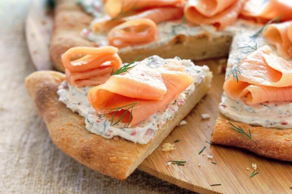 A smoked salmon pizza with cream cheese, red onion, and dill with one wedge cut out.