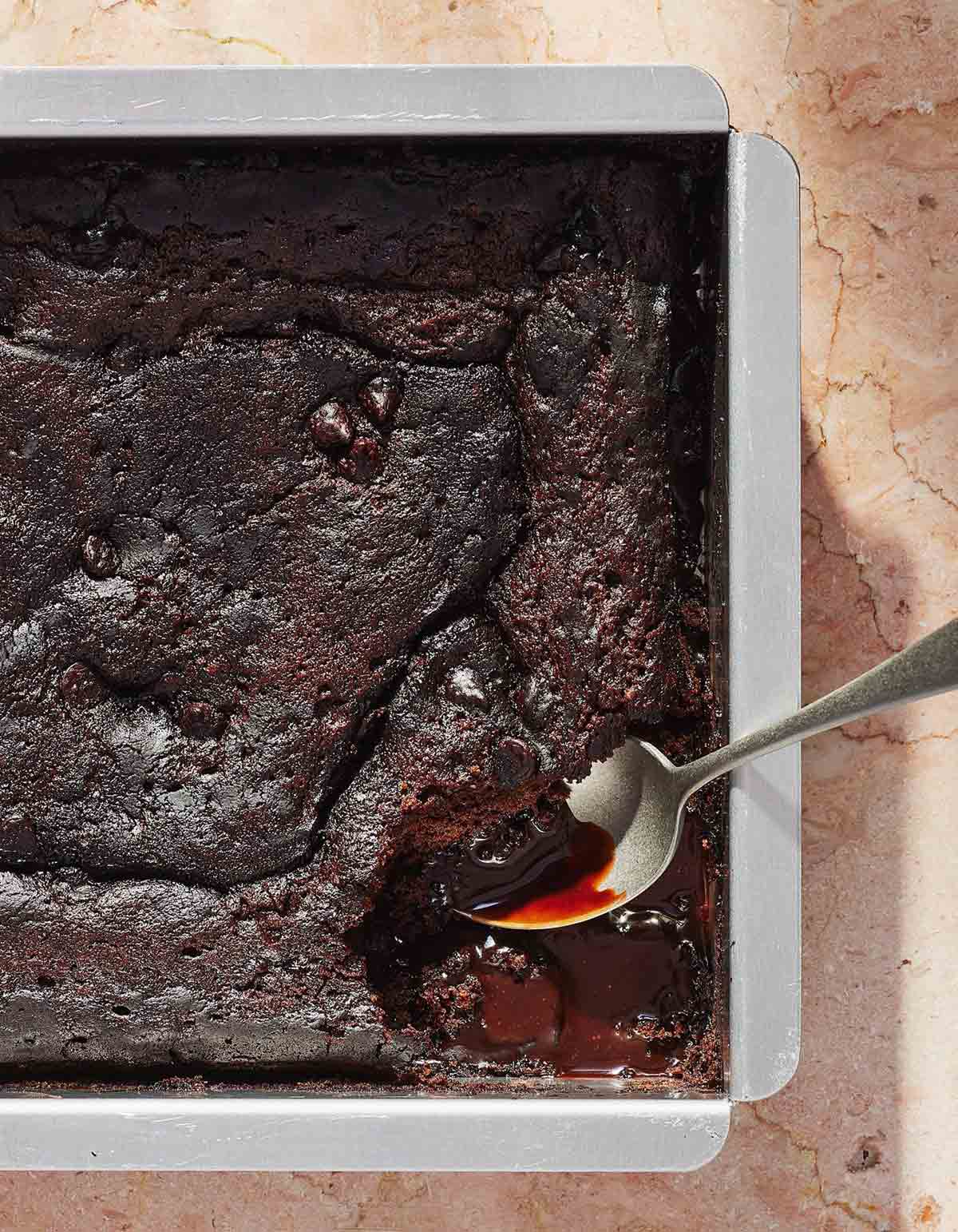 A baking dish filled with spicy hot fudge pudding cake and a spoon scooping out a portion.