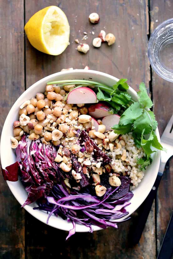 A veggie rice bowl filled with cabbage, rice, chickpeas, hazelnuts, and cilantro on a wooden table.