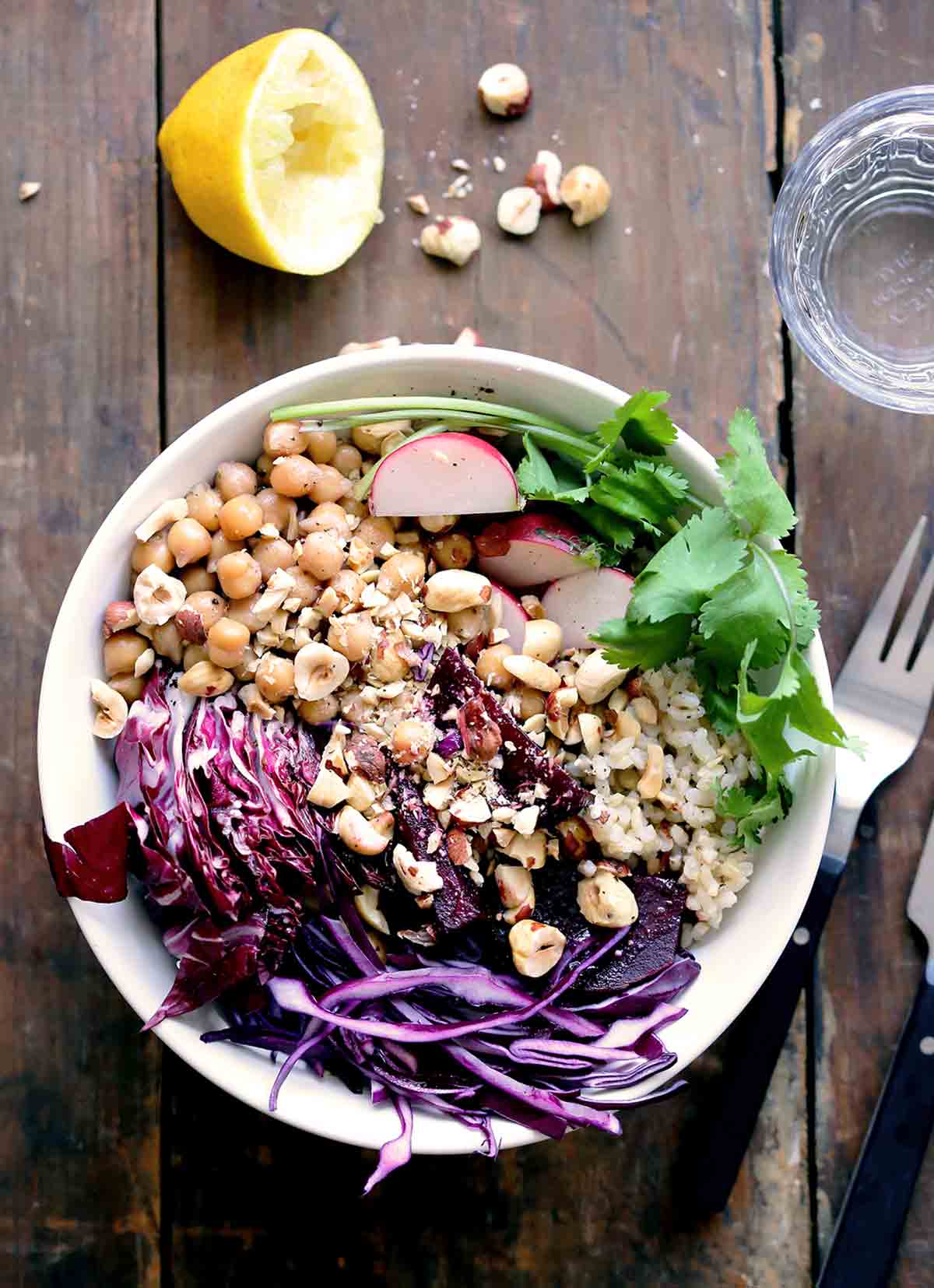 A veggie rice bowl filled with cabbage, rice, chickpeas, hazelnuts, and cilantro on a wooden table.