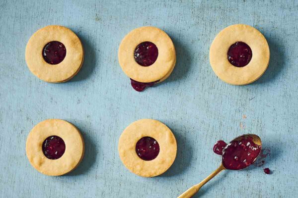 Five condensed milk cookie sandwiches filled with jam, with a spoonful of jam on the side.