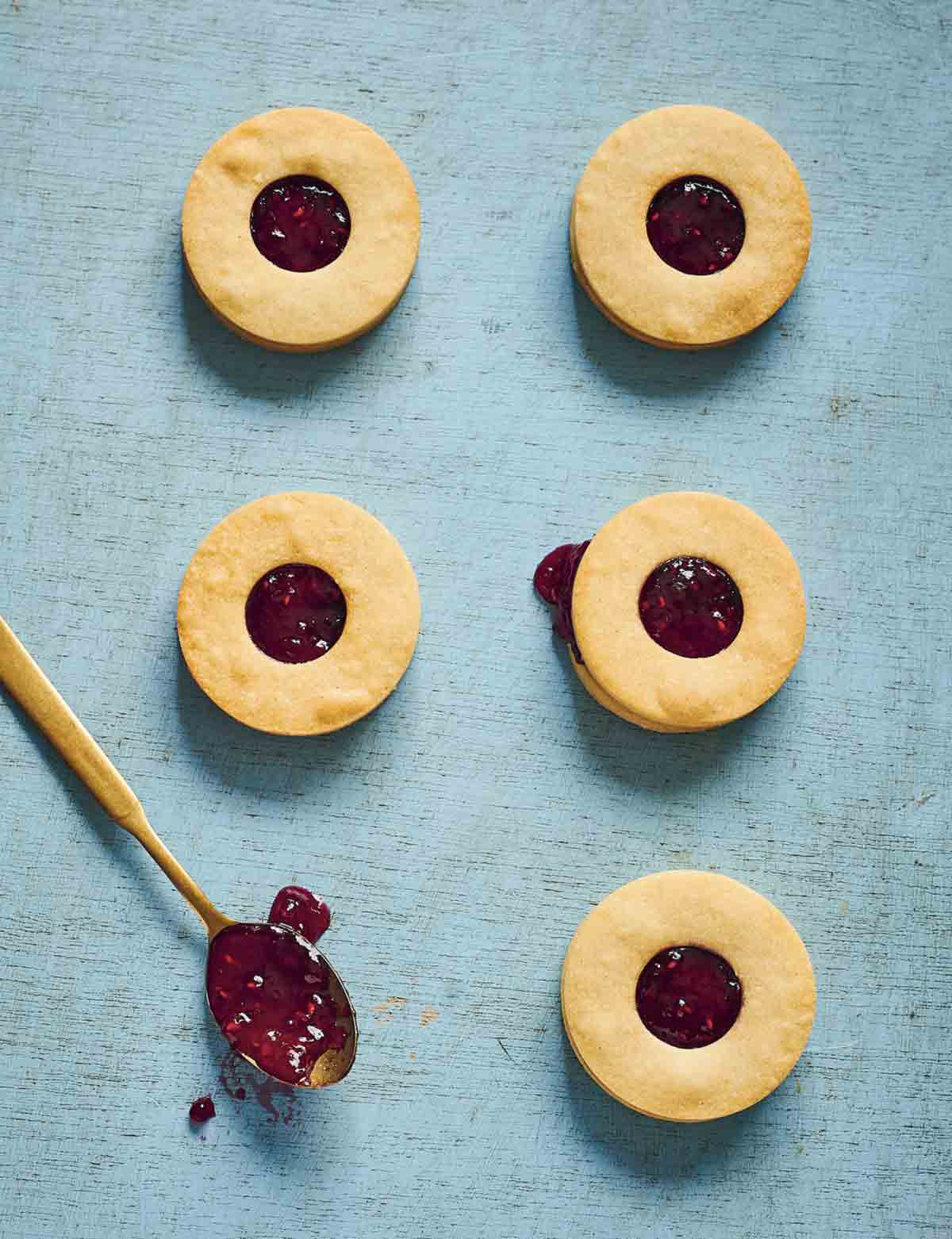 Five condensed milk cookie sandwiches filled with jam, with a spoonful of jam on the side.