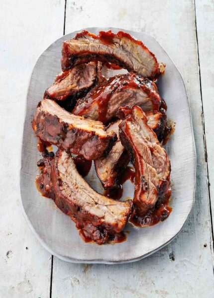 A white oval platter filled with individual baby back ribs with coca cola bbq sauce.