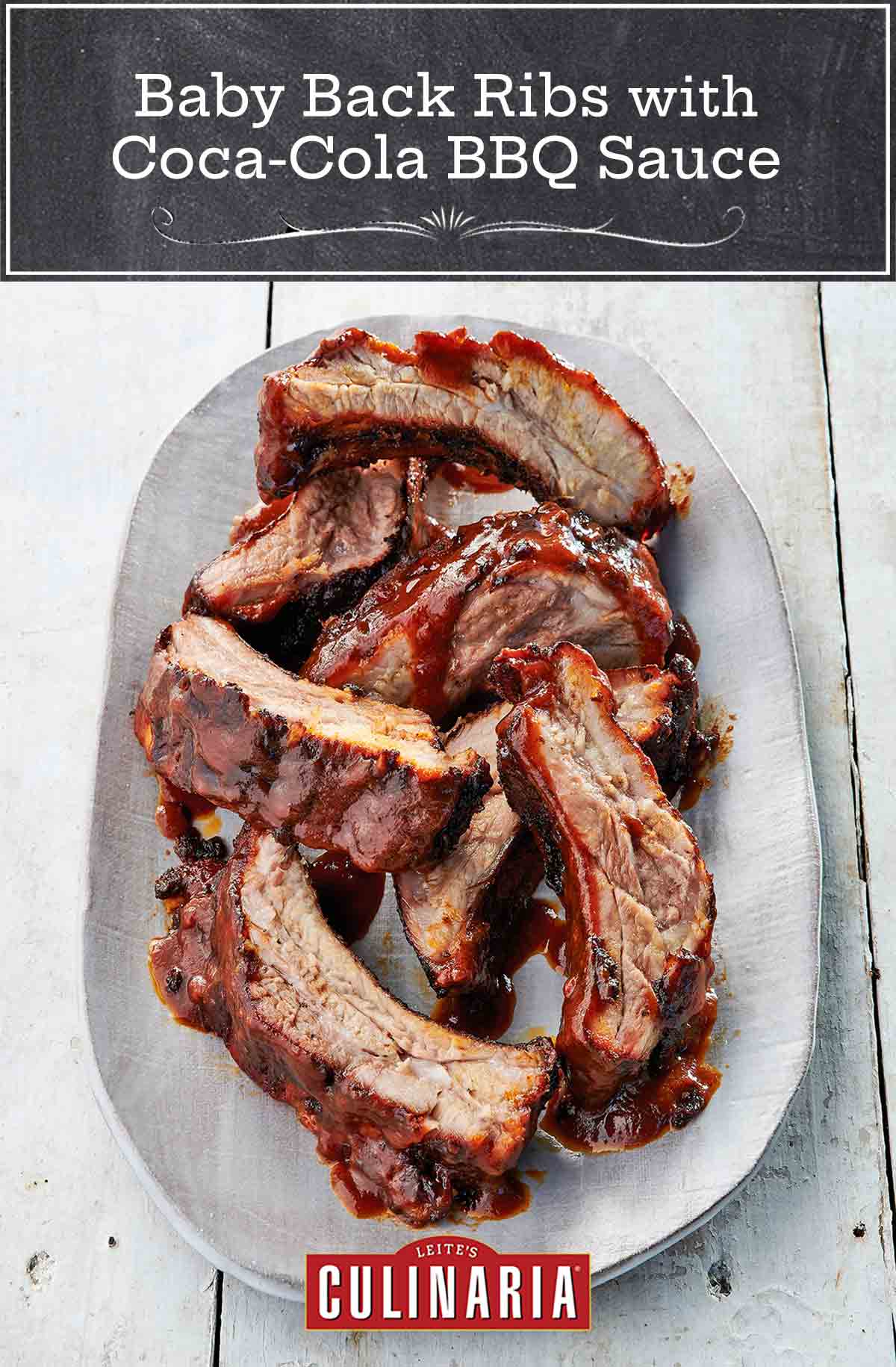 A white oval platter filled with individual baby back ribs with coca cola bbq sauce.