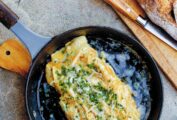 A black skillet containing a cheese omelet, topped with chives and Gruyere.