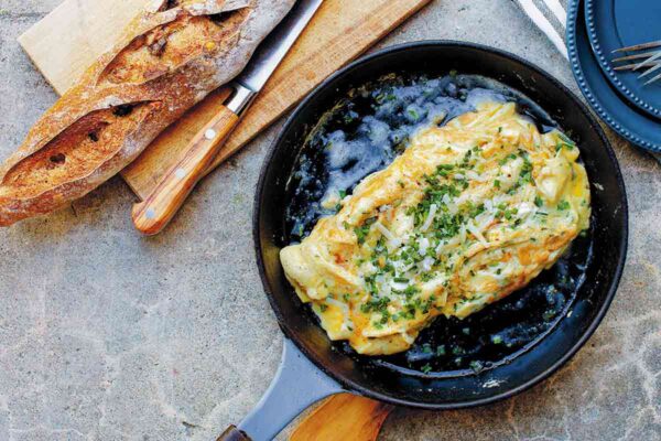 A black skillet containing a cheese omelet, topped with chives and Gruyere.