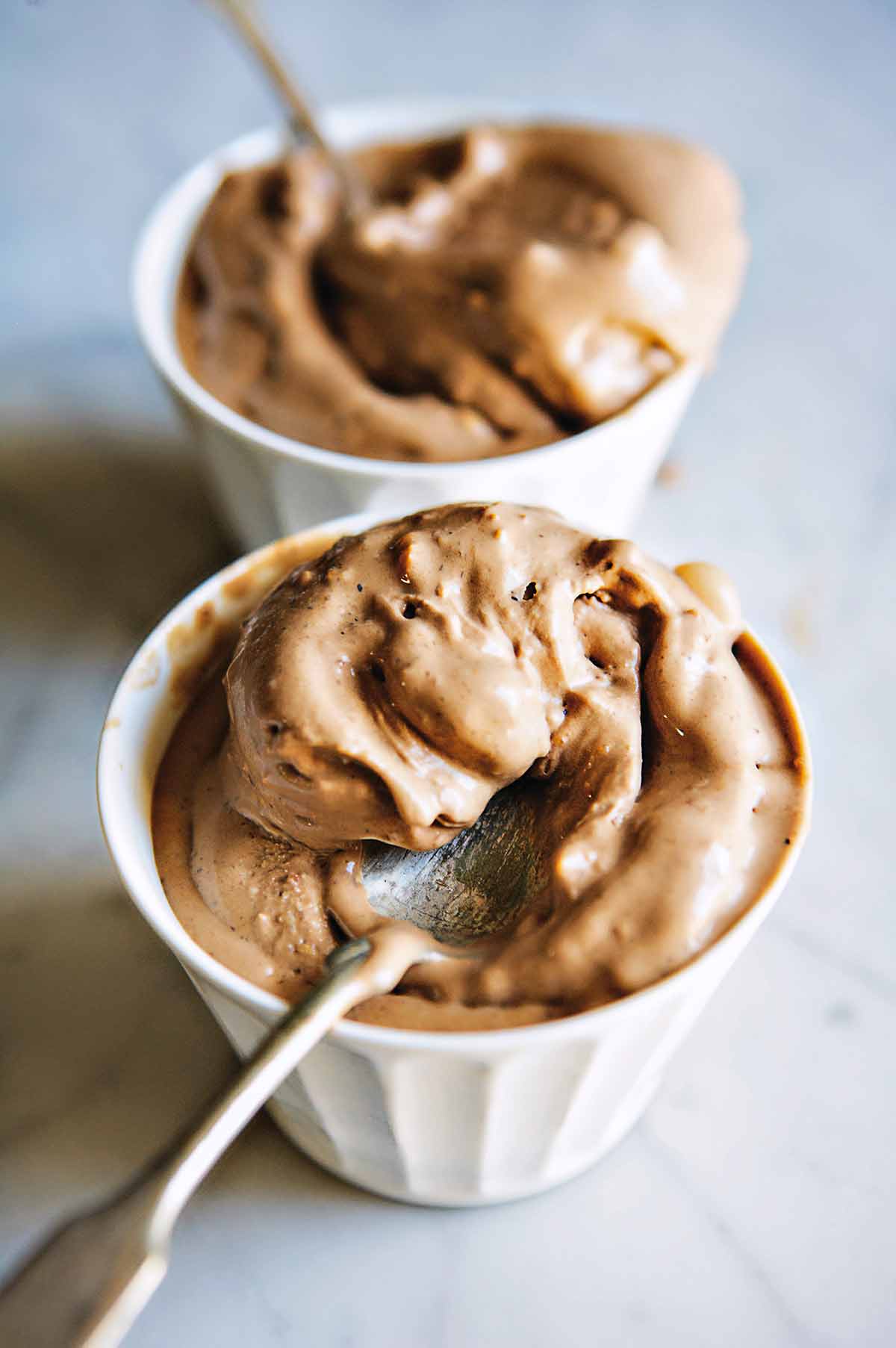 Two cups with scoops of chocolate hazelnut gelato, known as gelato di gianduia, with a spoon.