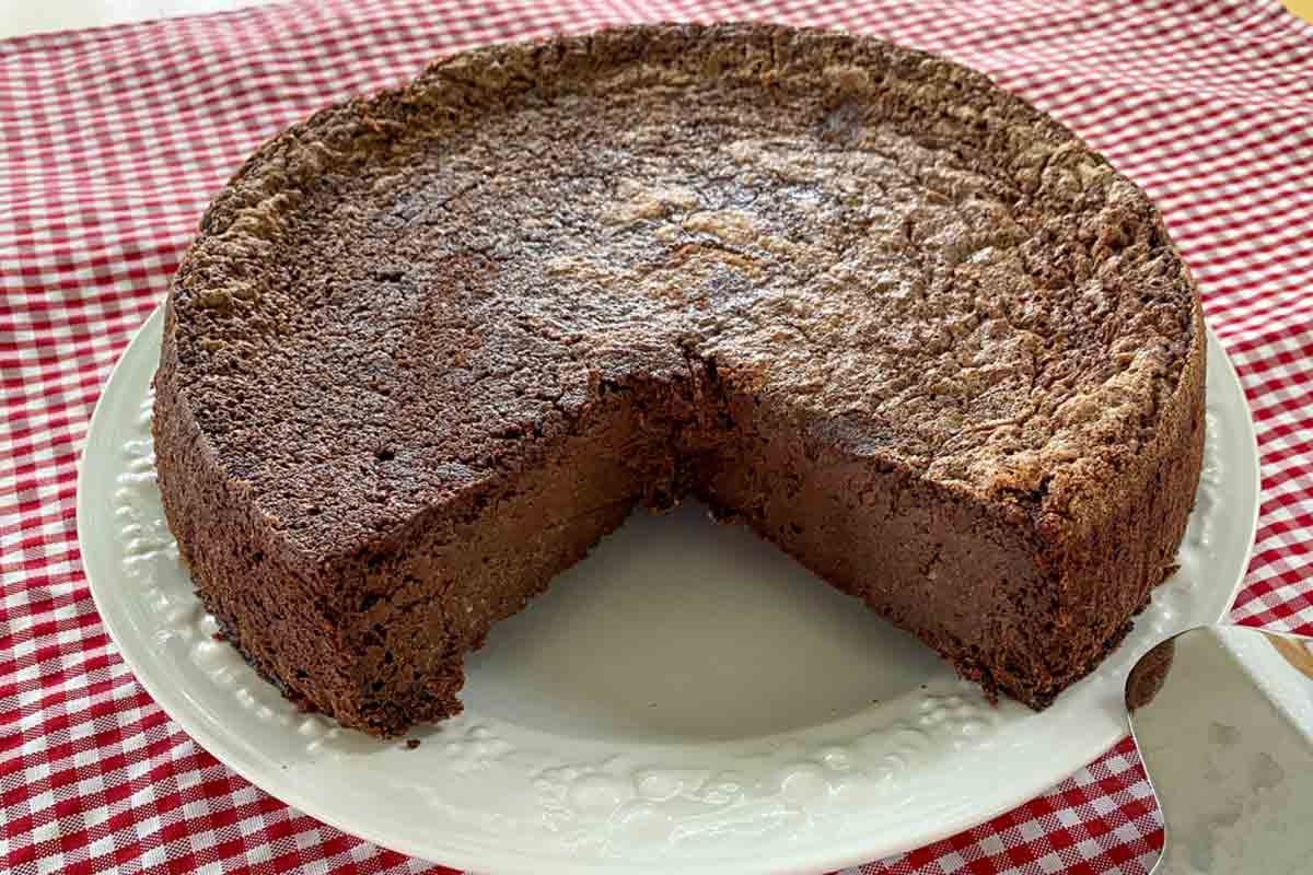 A round chocolate polenta pudding cake on a white plate with one slice cut from it.